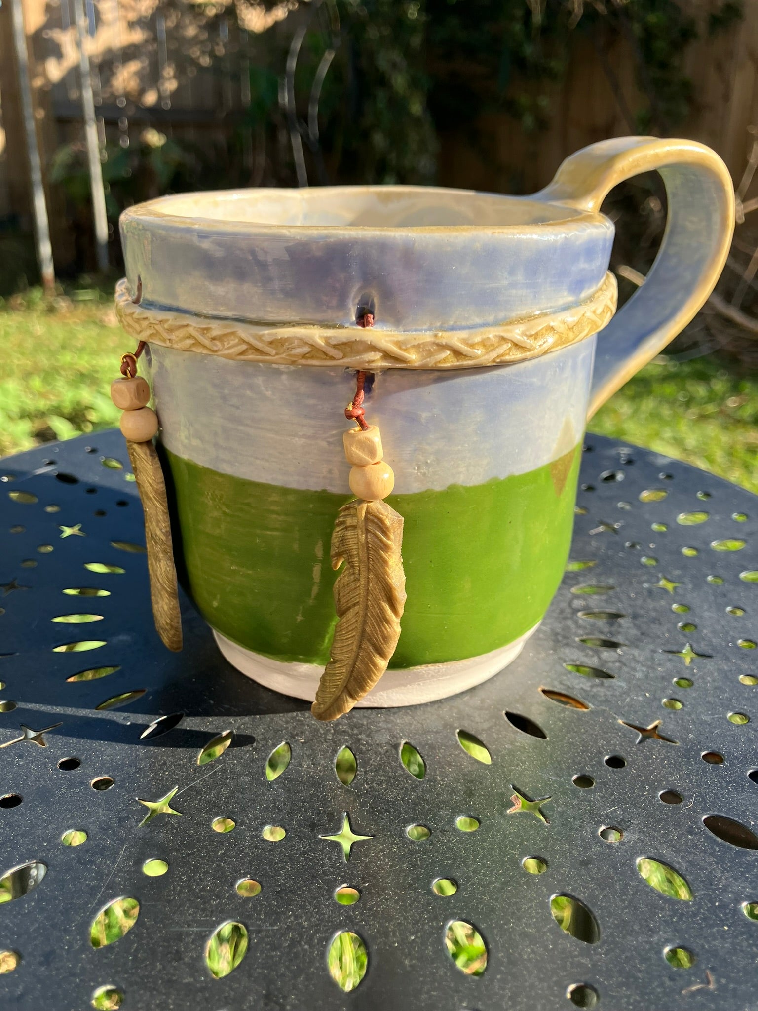 Handcrafted Dreamkeeper Mug with sculpted hanging feathers, blue & green glaze, and braided band detail, handmade pottery by Dhess Pottery