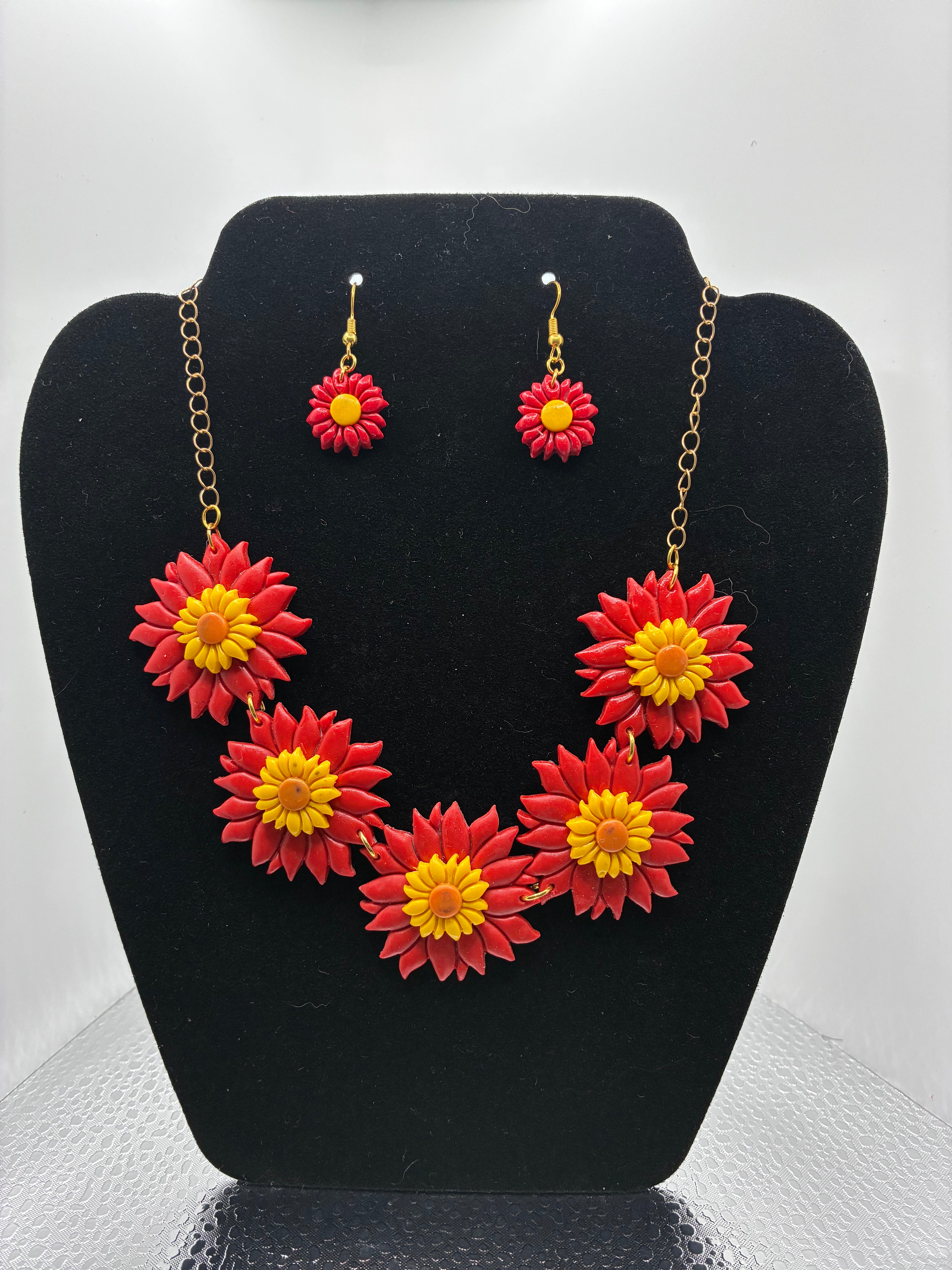 Floral necklace and earrings set on a black stand with a white background