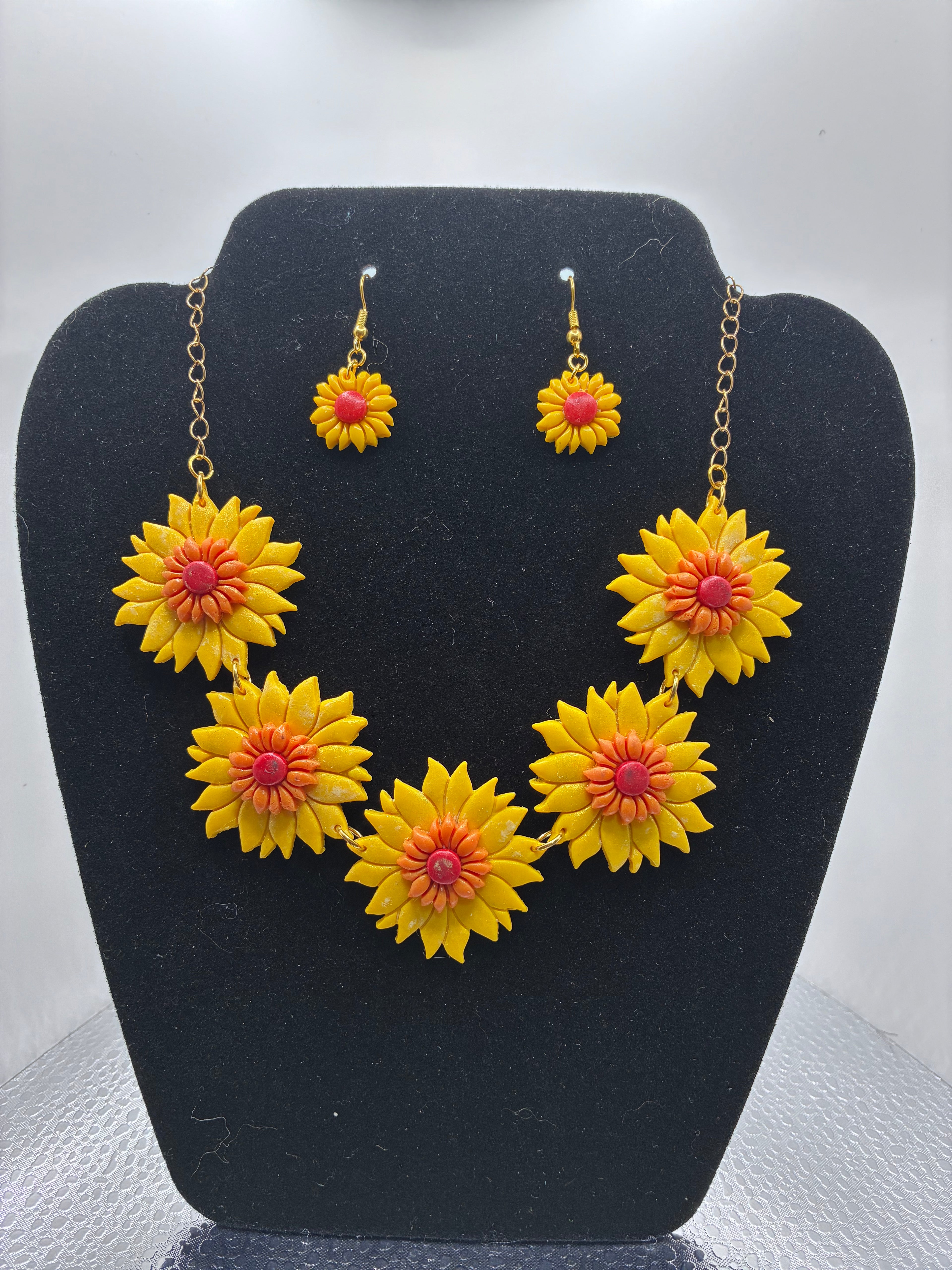 Jewelry set with yellow flower-shaped earrings and necklace on a black stand.
