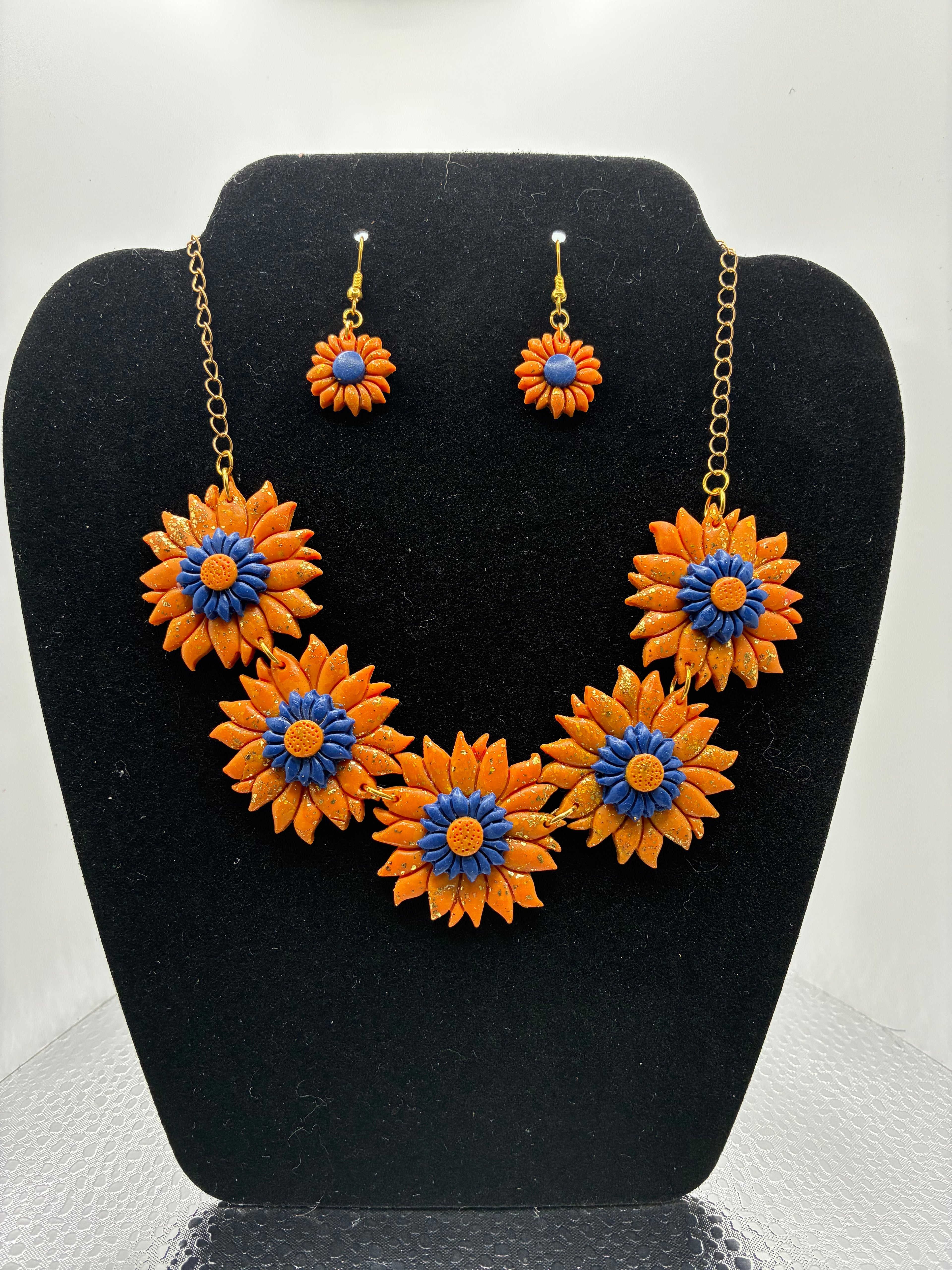 Floral jewelry set with orange and blue flowers on a black stand.
