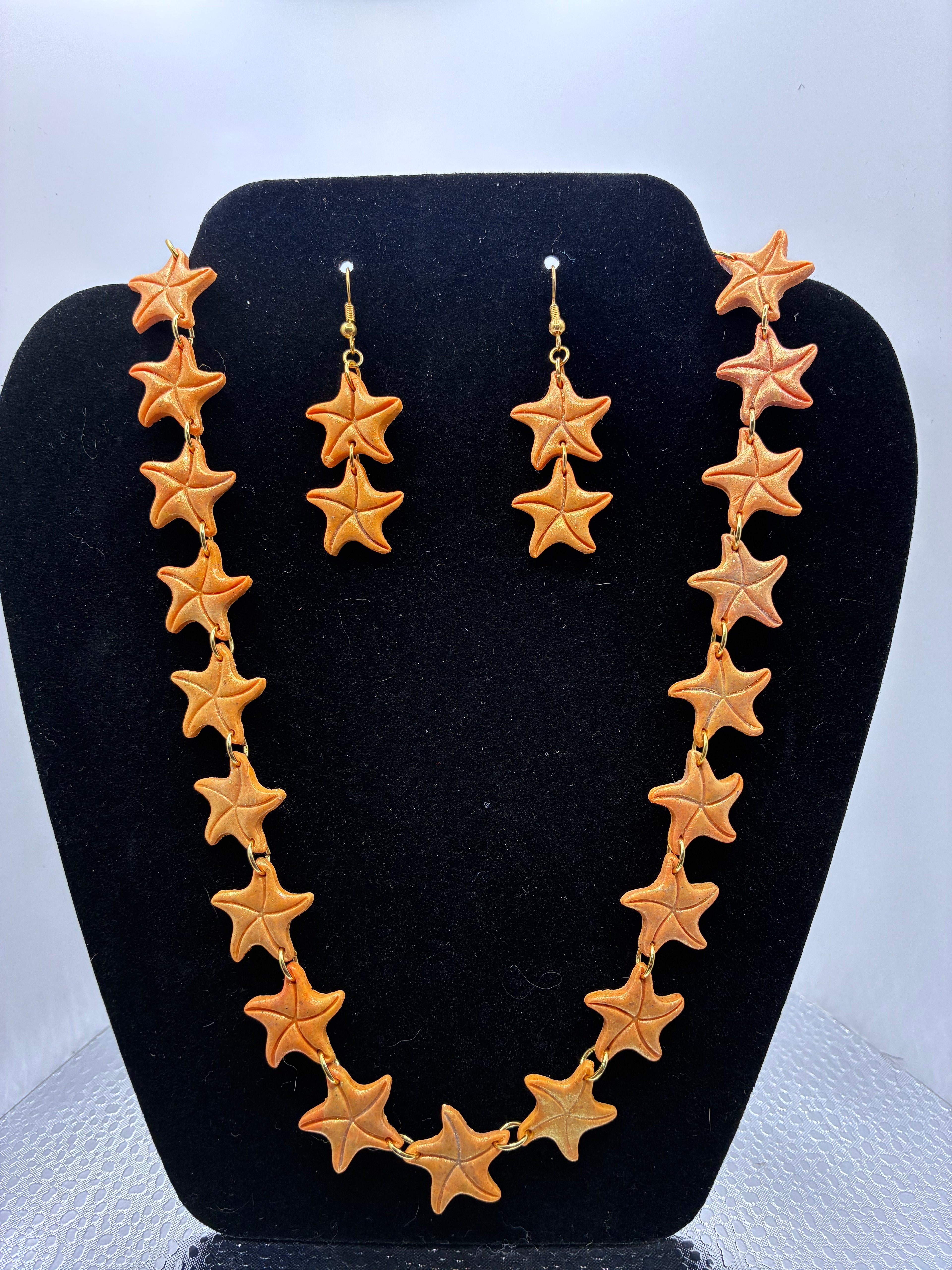 Gold star necklace and earrings on a black stand against a white background