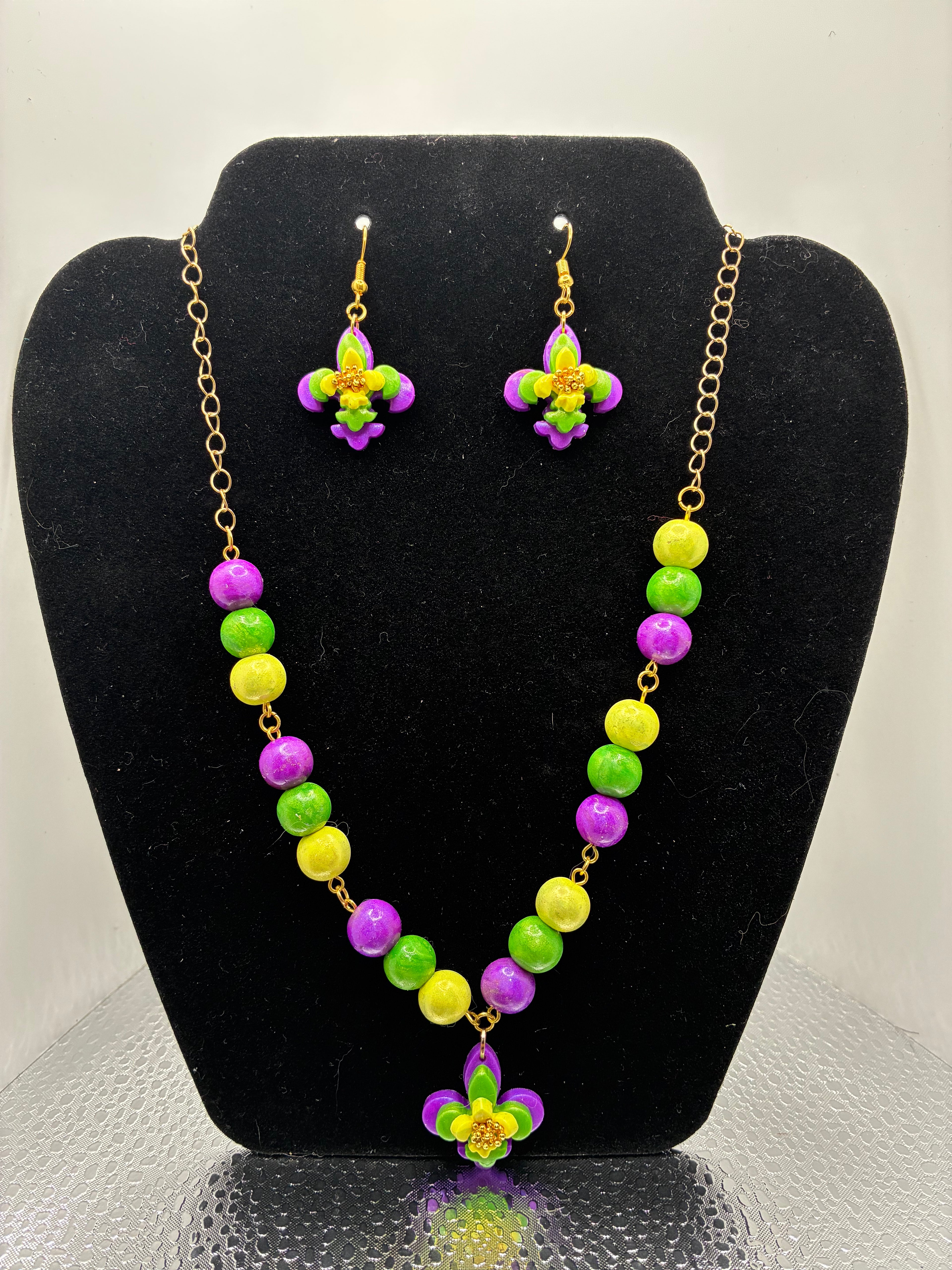 Necklace and earrings set with green, purple, and yellow beads on a black stand.