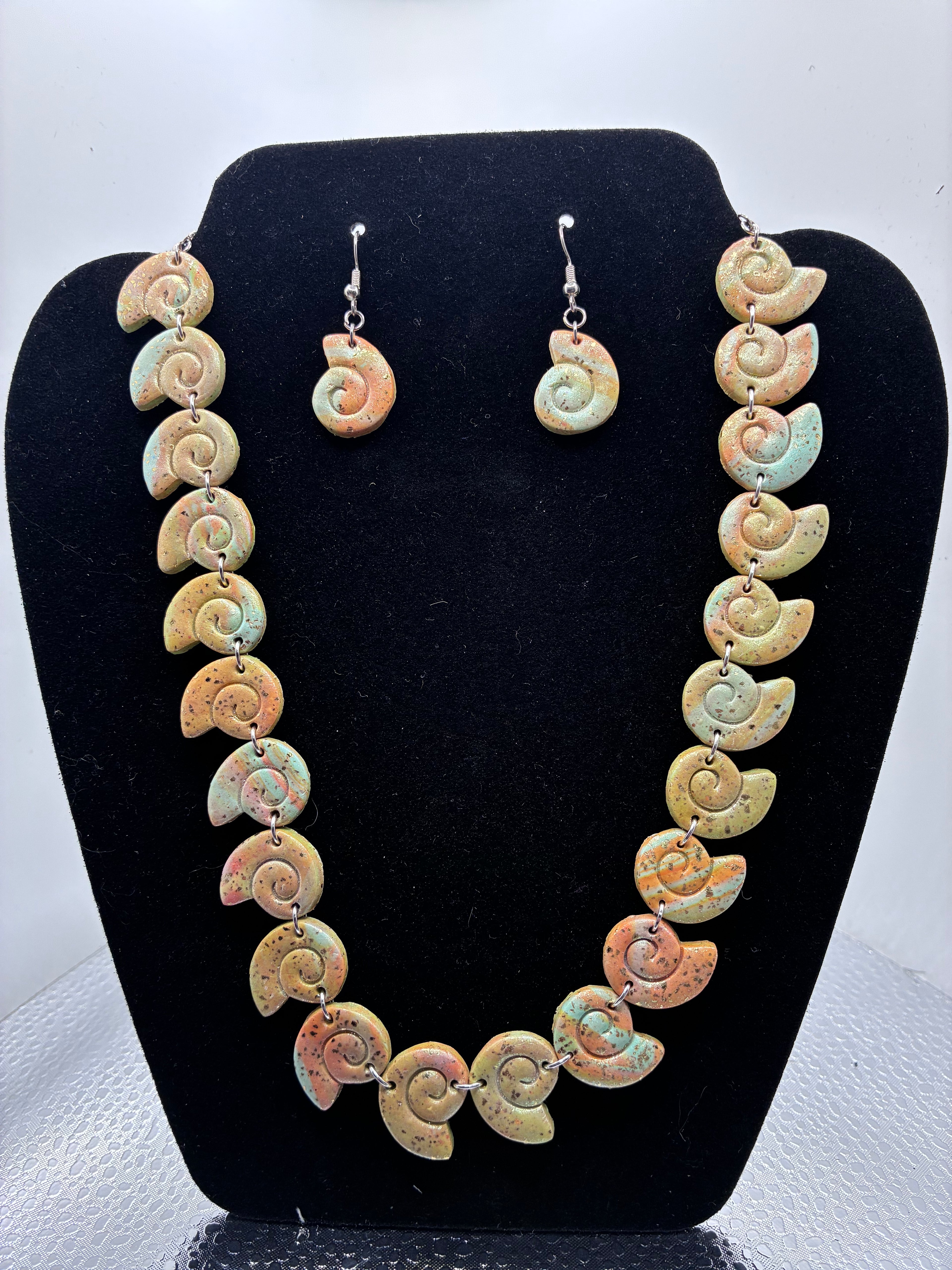 Necklace and earrings with shell design on a black stand