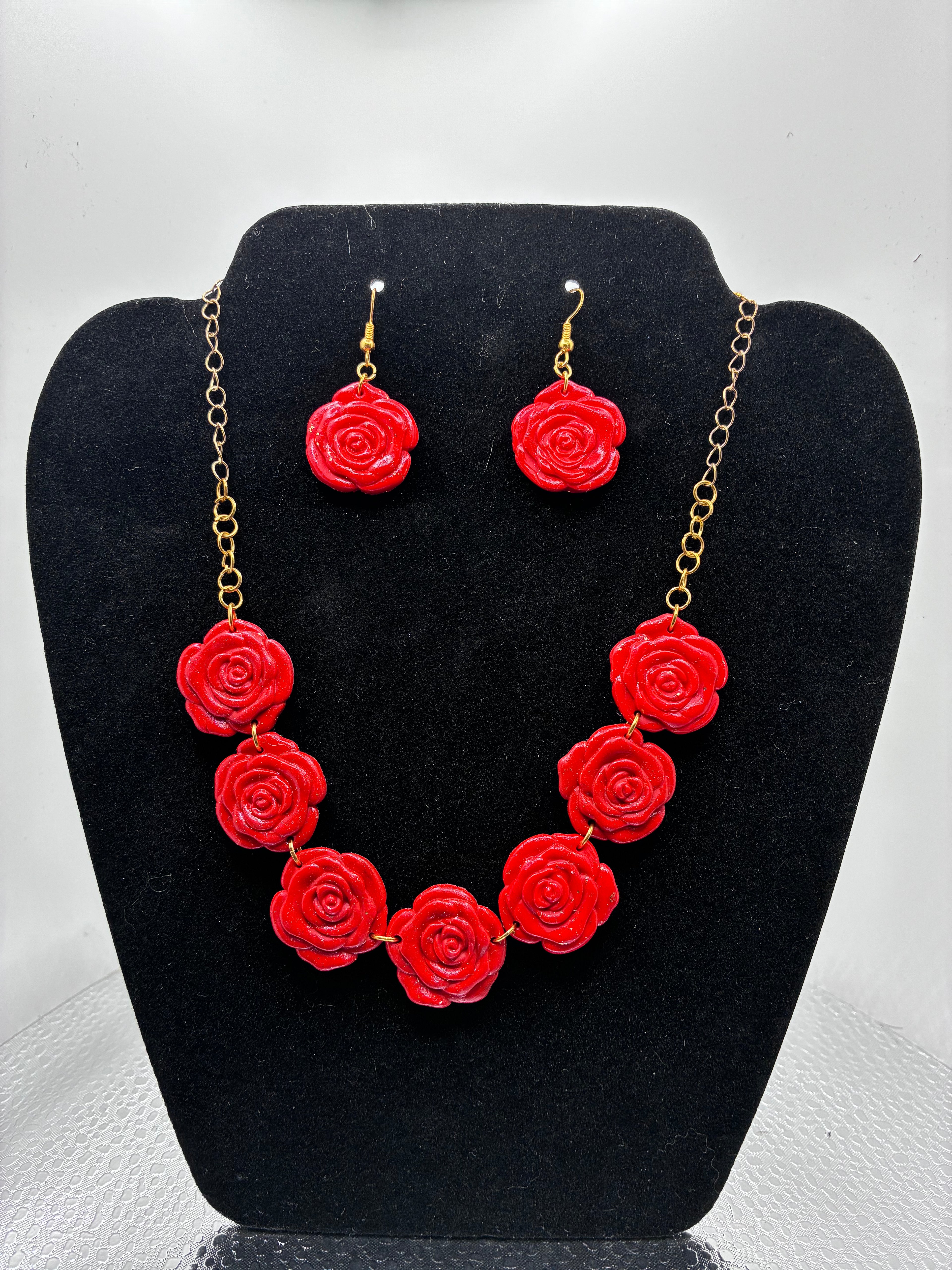 Red rose necklace and earrings on a black stand with a white background