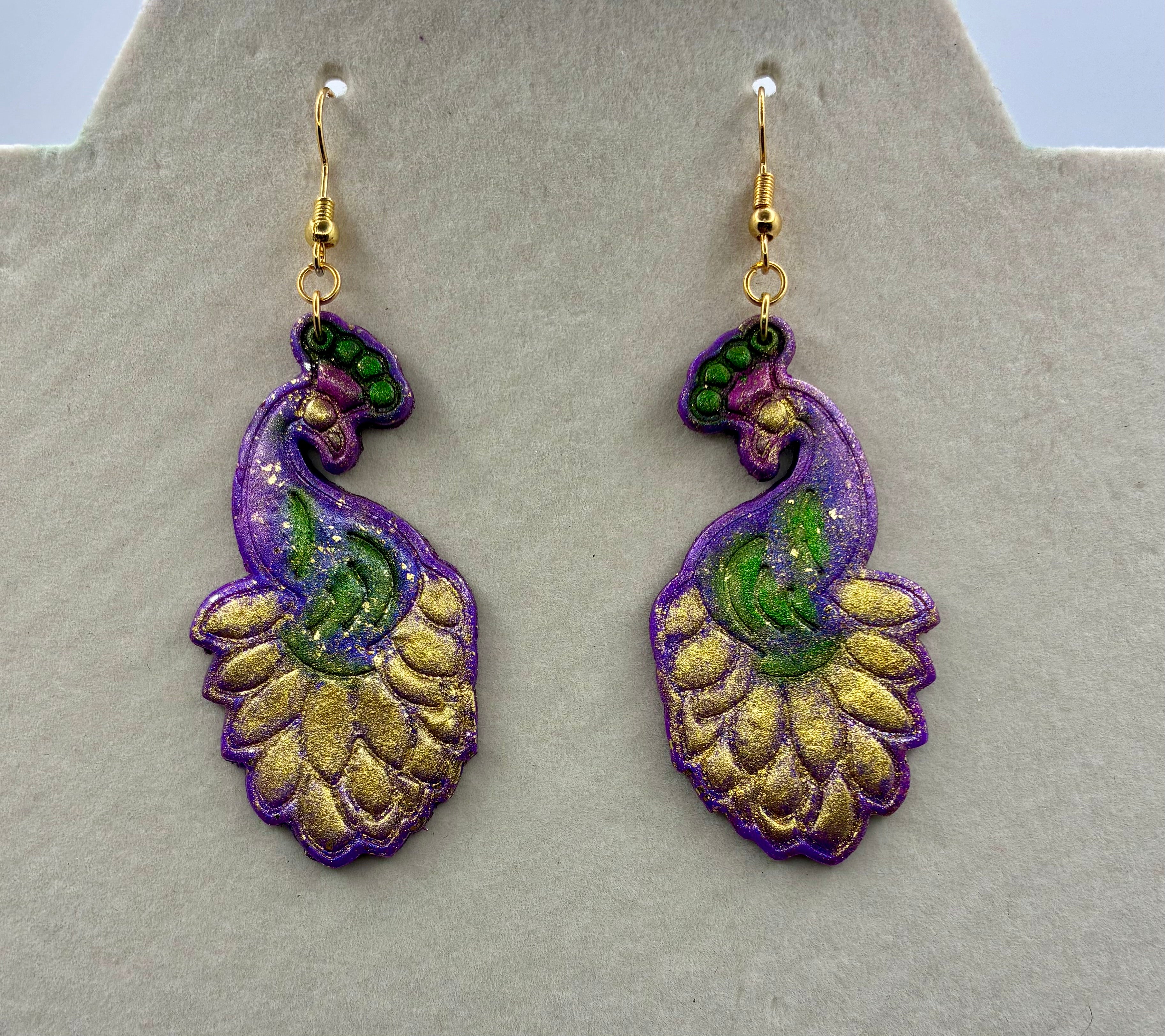 Pair of decorative earrings with purple, gold, and green design on a gray background