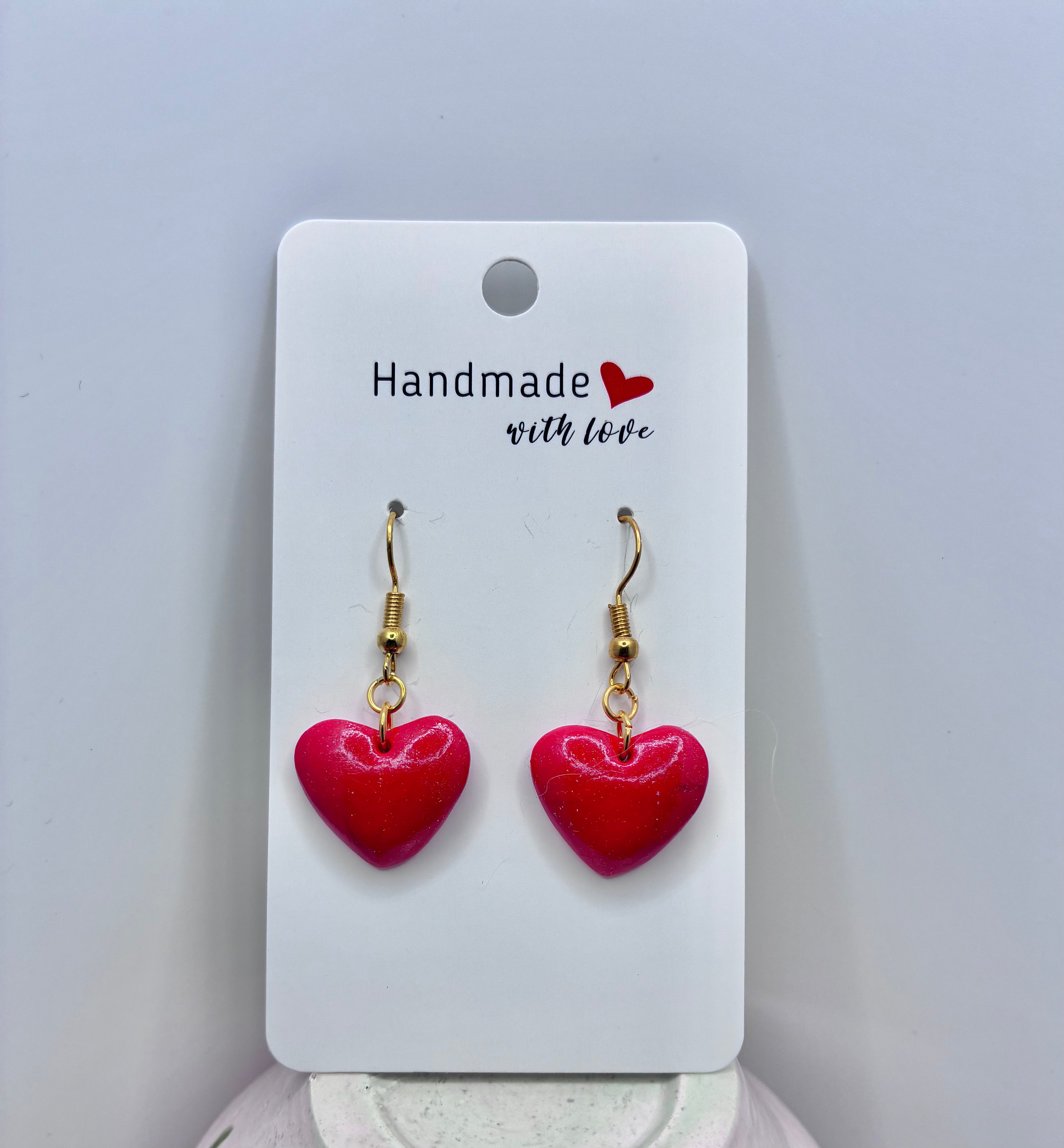 Heart-shaped earrings on a 'Handmade with Love' card against a gray background