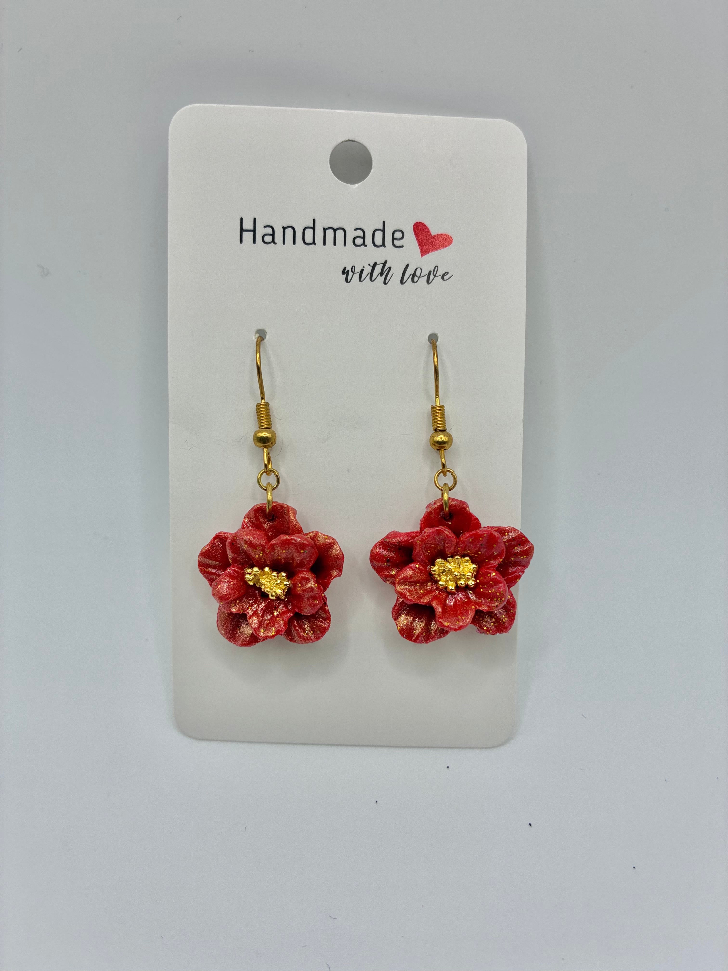 Red flower-shaped earrings on a 'Handmade with Love' card against a gray background