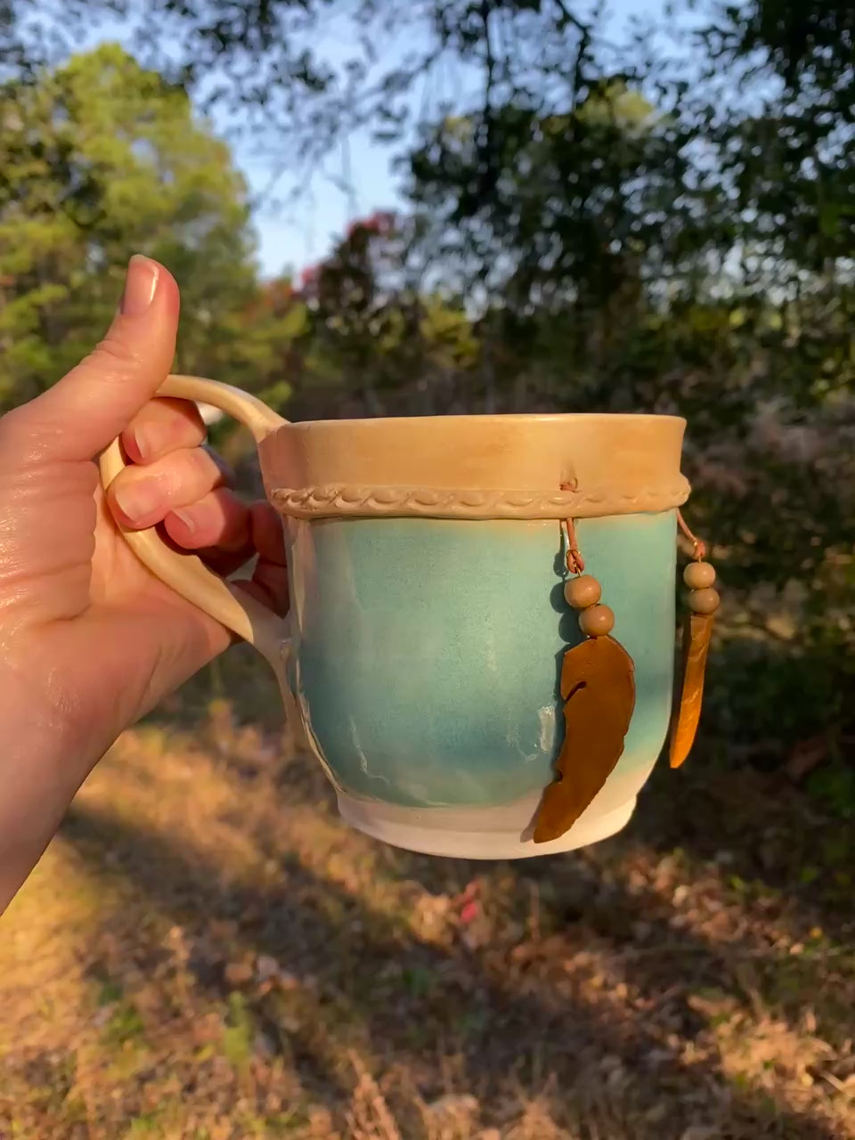 Handcrafted Dreamkeeper Mug with sculpted hanging feathers, turquoise glaze, and braided band detail, handmade pottery by Dhess Pottery